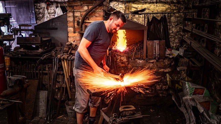 Blacksmith sends sparks flying at the anvil inside at Branscombe, Devon